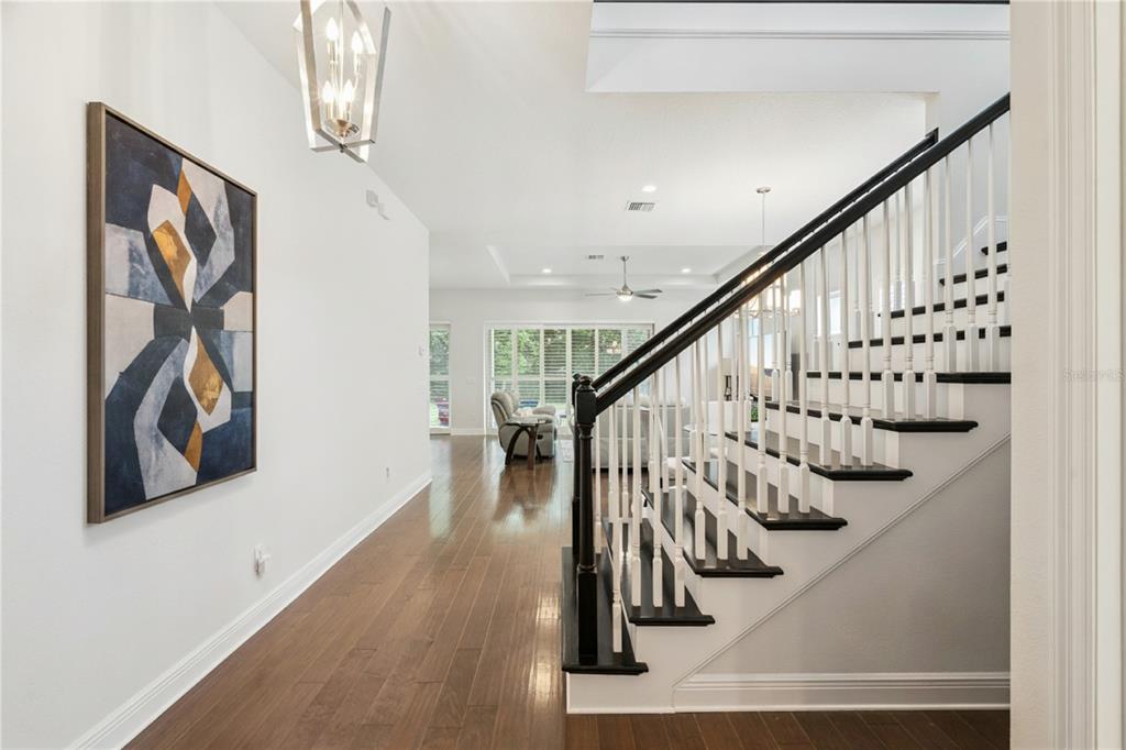 A bright entryway features hardwood floors, a staircase with black treads, and a modern chandelier — 15709 SHOREBIRD LANE, WINTER GARDEN, FL