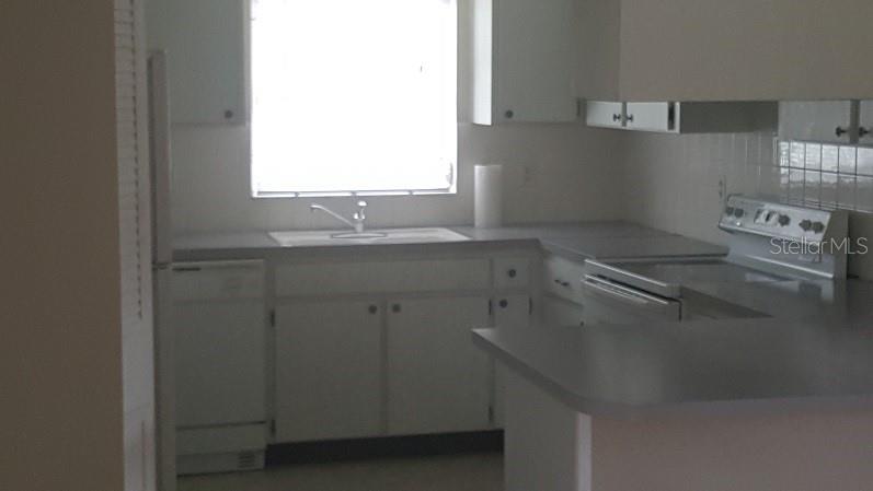 A kitchen with white cabinets, gray countertops, a sink under a window, and white appliances — 1250 S PINELLAS AVENUE UNIT 809, TARPON SPRINGS, FL