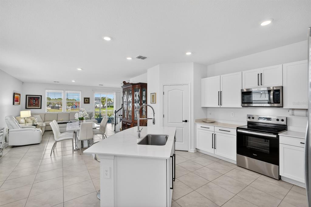 A bright open-concept kitchen with white cabinets, a center island, and an adjacent dining area — 336 REDBUD ROAD, PALM COAST, FL