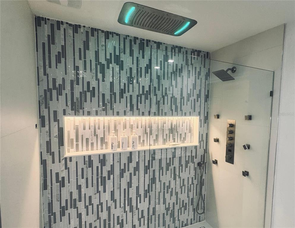 A modern shower features a rainfall head with LED lighting, body jets, and tiled walls — 336 REDBUD ROAD, PALM COAST, FL