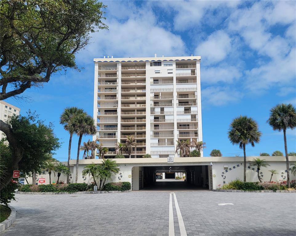 A multi-story residential building features balconies and a ground-level parking entrance under a blue sky — 750 N ATLANTIC AVENUE UNIT 1104, COCOA BEACH, FL