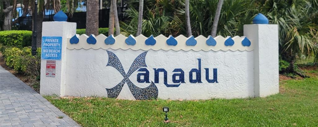 A white stucco sign with blue mosaic lettering reads Xanadu in front of tropical landscaping — 750 N ATLANTIC AVENUE UNIT 1104, COCOA BEACH, FL