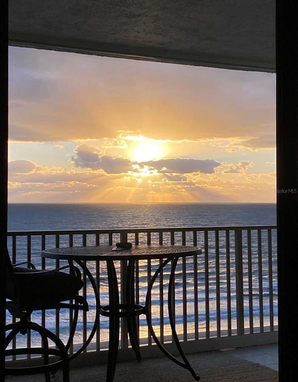 A balcony with a table and chair overlooks the ocean during a sunset — 750 N ATLANTIC AVENUE UNIT 1104, COCOA BEACH, FL