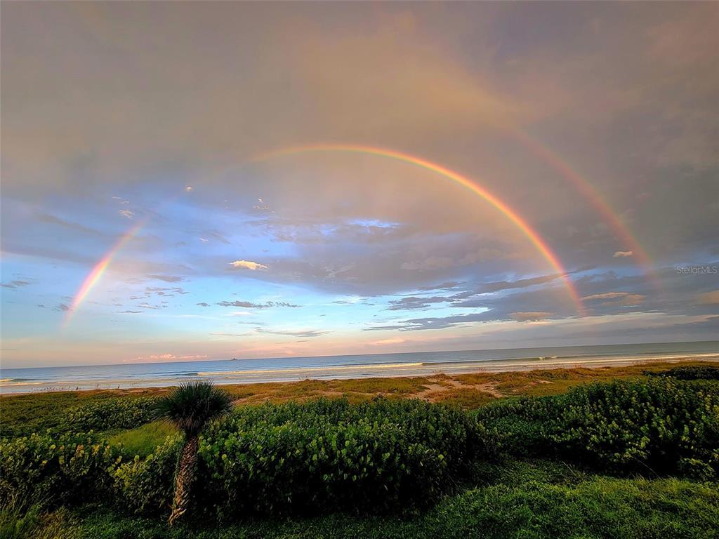 A double rainbow arches over a beach with green vegetation in the foreground — 750 N ATLANTIC AVENUE UNIT 1104, COCOA BEACH, FL