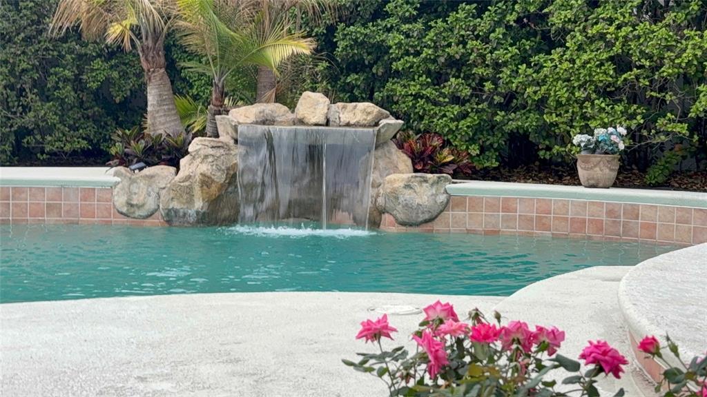 A swimming pool features a rock waterfall, tiled coping, and surrounding tropical landscaping — 9115 BAY SIDE COURT, ORLANDO, FL