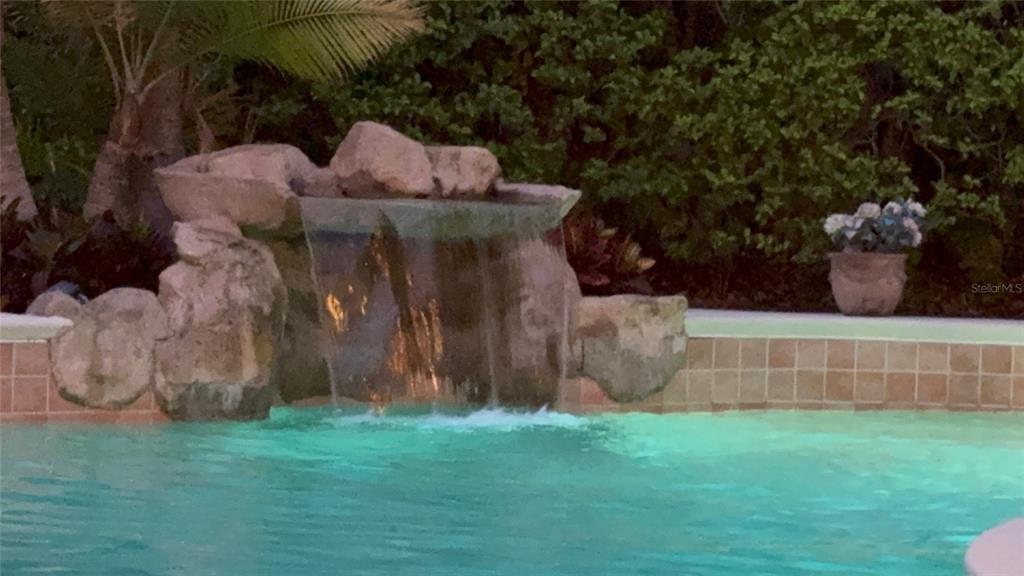 A stone waterfall feature cascades into a swimming pool with tan tiled coping — 9115 BAY SIDE COURT, ORLANDO, FL