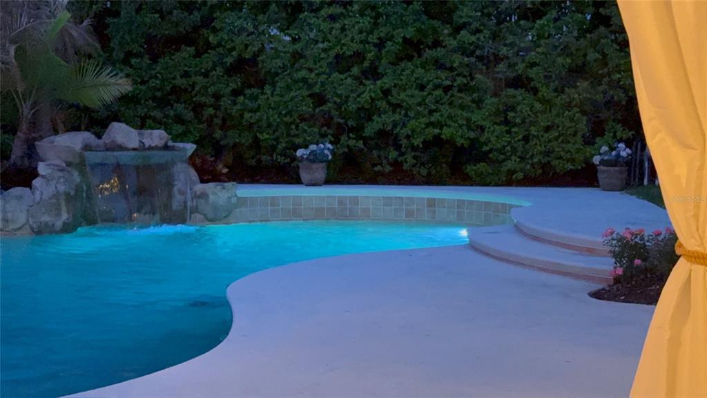 A swimming pool with a rock waterfall feature and a concrete deck at dusk — 9115 BAY SIDE COURT, ORLANDO, FL