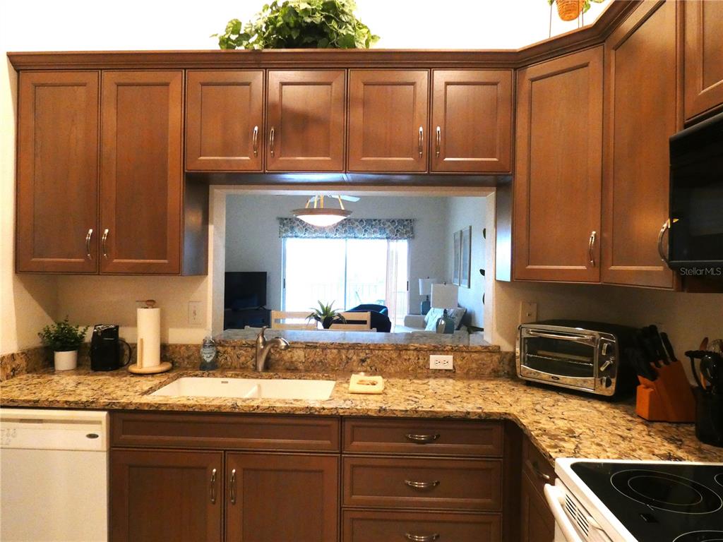 A kitchen with brown cabinets, granite countertops, and a pass-through window to the living area — 9300 CLUBSIDE CIRCLE UNIT 1307, SARASOTA, FL