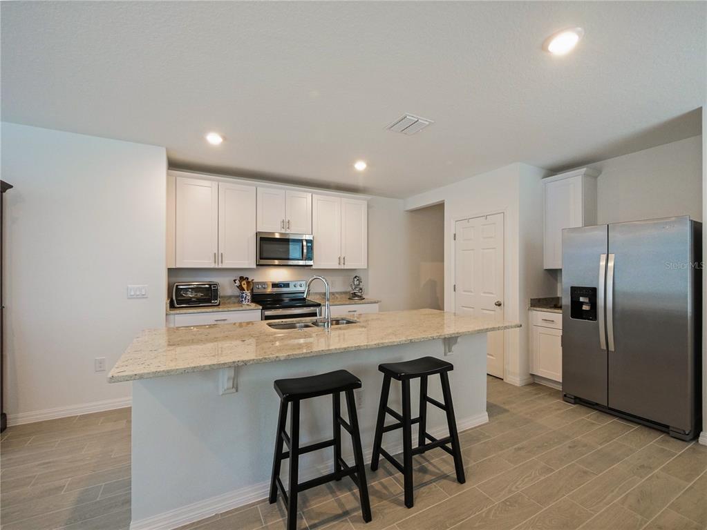 A kitchen features white cabinets, granite countertops, a center island with stools, and stainless appliances — 4847 RIGGING ST, HAINES CITY, FL
