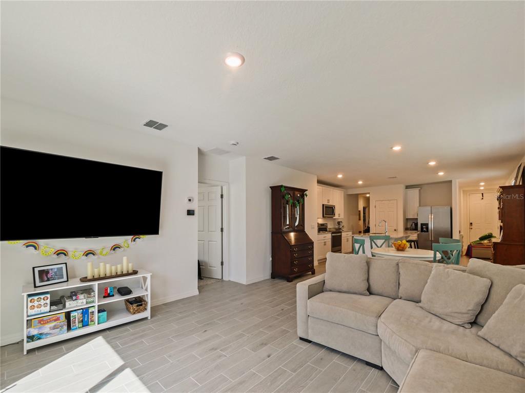 A living room with a large television, sectional sofa, and an open kitchen beyond — 4847 RIGGING ST, HAINES CITY, FL