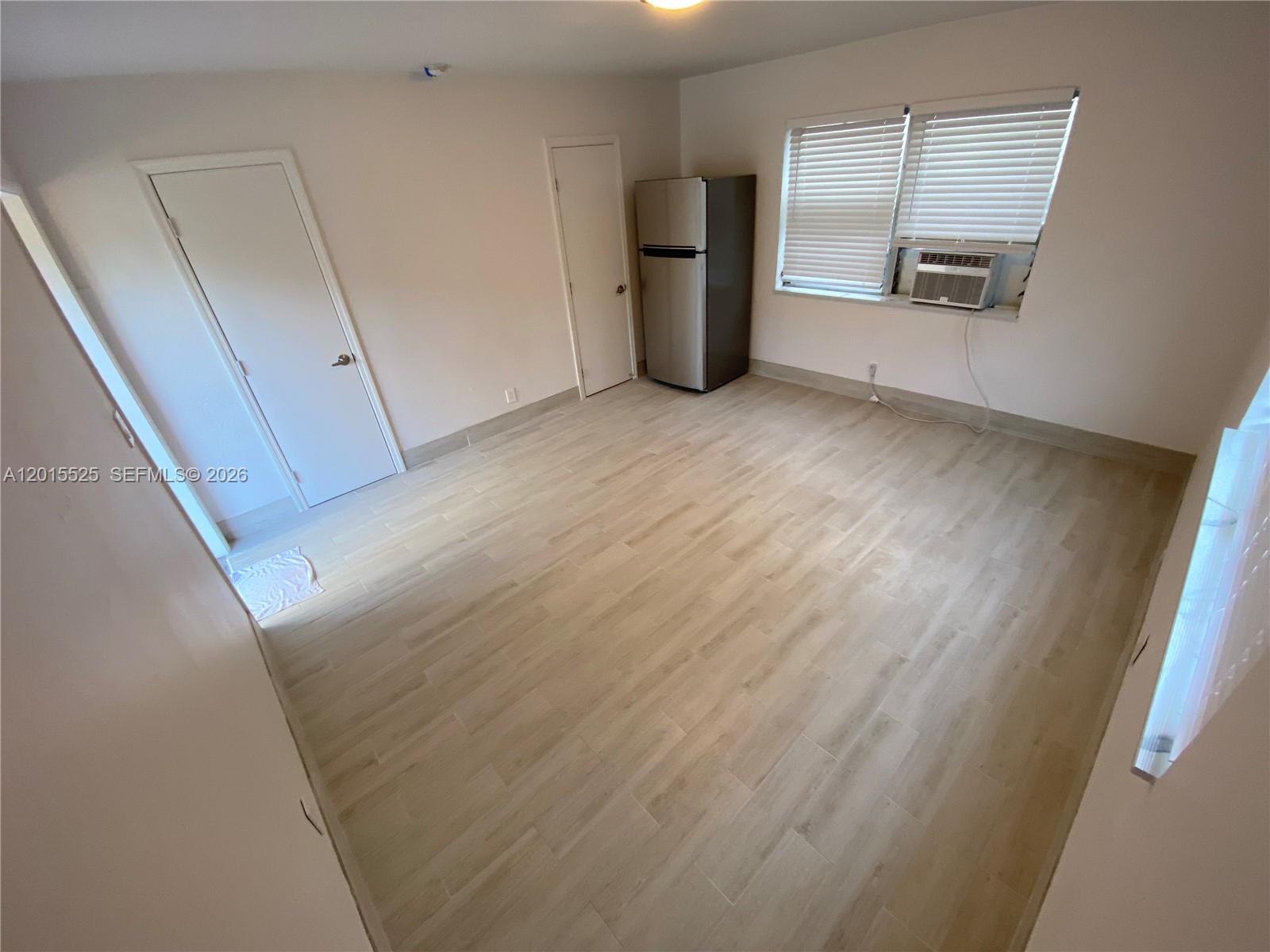 An empty room features light wood-look flooring, two white doors, and a window air conditioner — 1723 Liberty St # 6, Hollywood FL 33020, HOLLYWOOD, FL