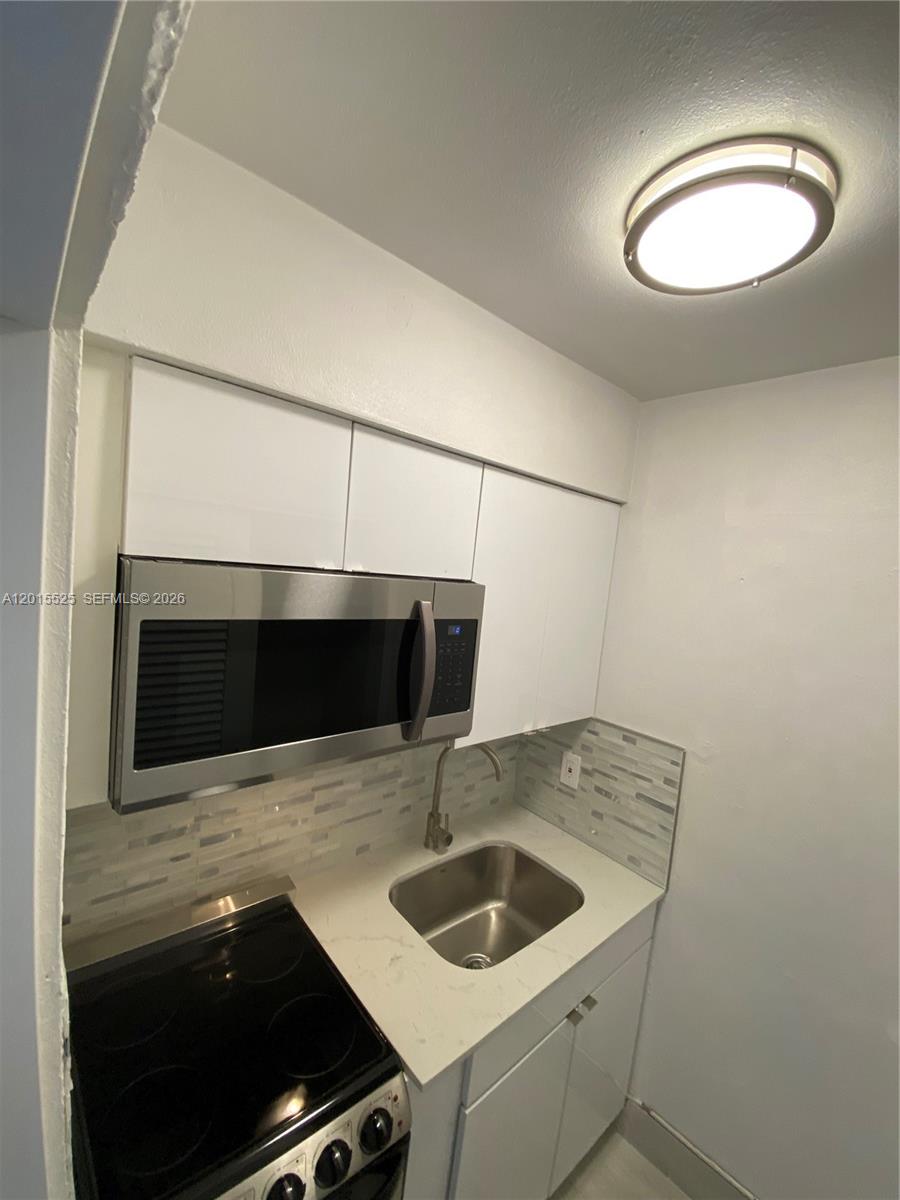 A compact kitchen features white cabinets, a stainless steel microwave, and a small sink — 1723 Liberty St # 6, Hollywood FL 33020, HOLLYWOOD, FL