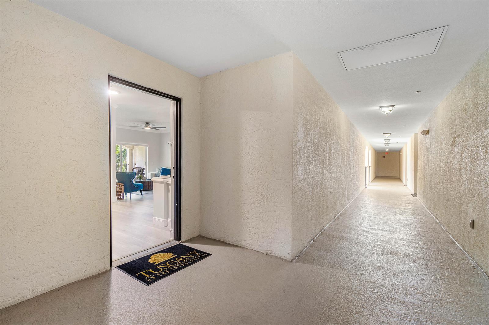An open doorway leads from a long, beige hallway into a bright, furnished apartment interior — 2408 Tuscany Way # 2408, Boynton Beach FL 33435, BOYNTON BEACH, FL