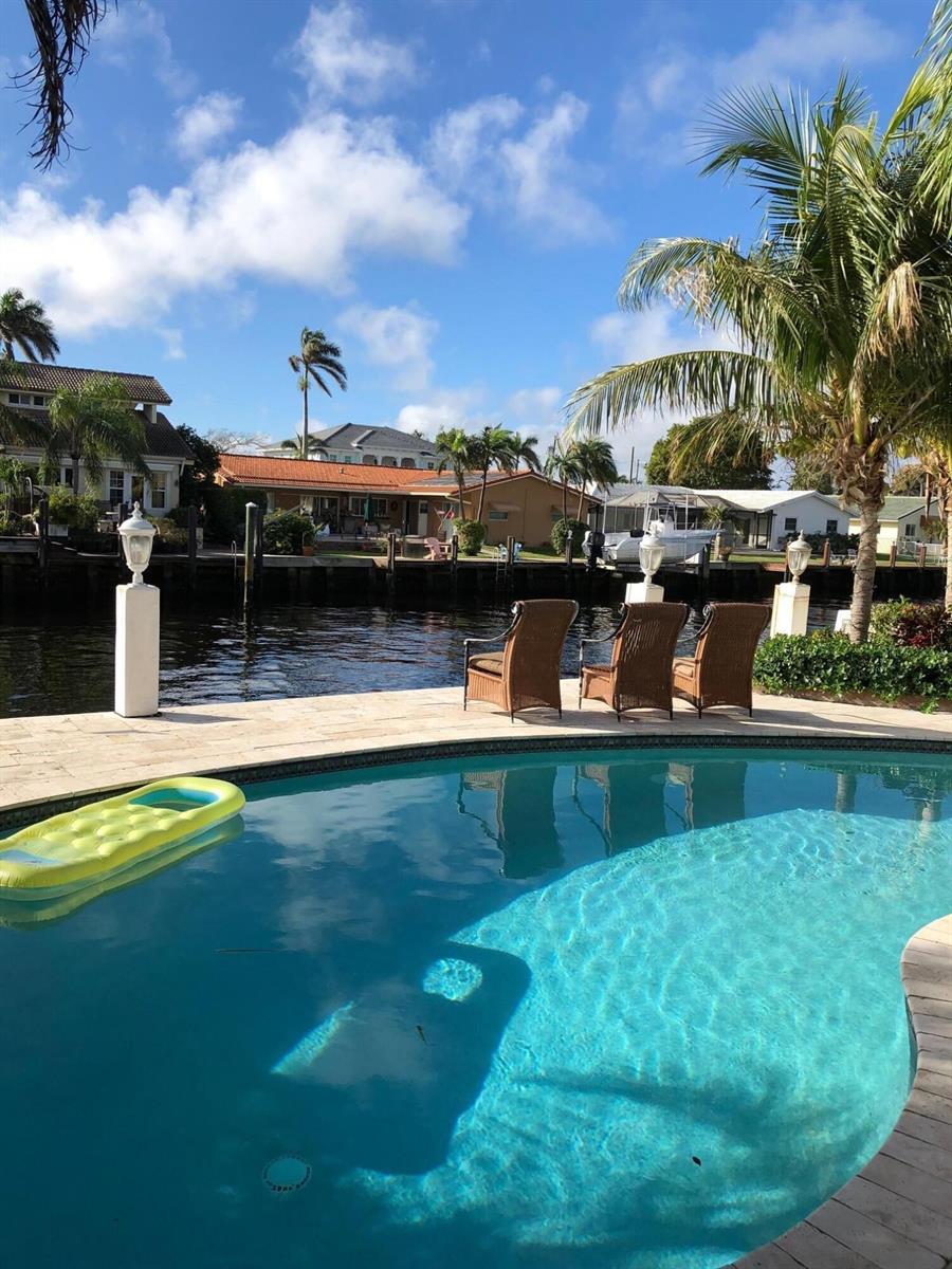 A swimming pool overlooks a canal with outdoor seating and houses in the background — 2740 NE 10th Street, Pompano Beach FL 33062, POMPANO BEACH, FL