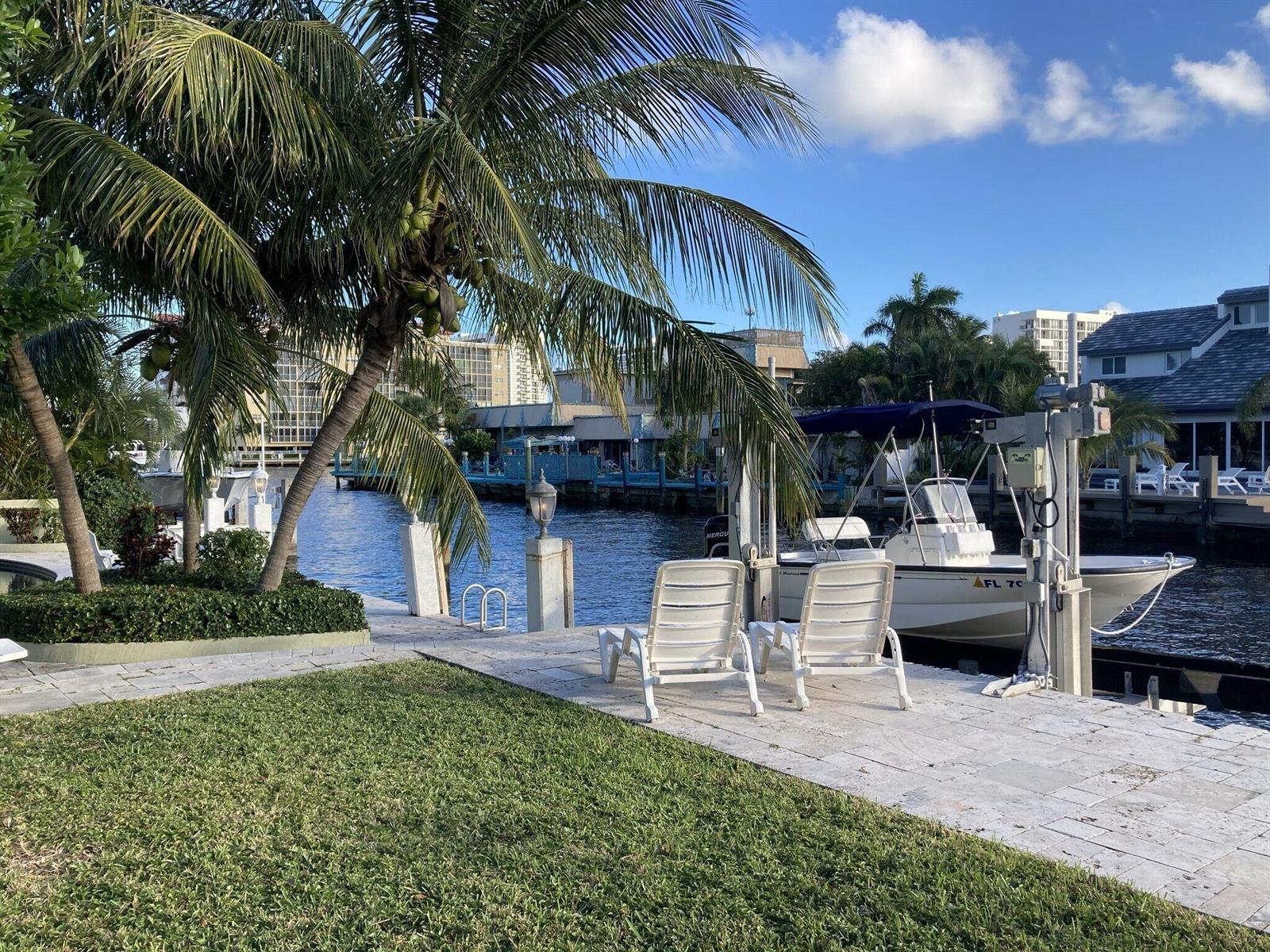 Two white lounge chairs sit on a stone patio beside a canal with a boat — 2740 NE 10th Street, Pompano Beach FL 33062, POMPANO BEACH, FL