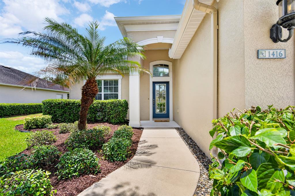 A concrete walkway leads to the blue front door of a beige stucco house — 1416 HICKORY VIEW CIRCLE, PARRISH, FL