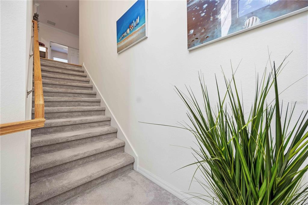 A carpeted staircase with a wooden handrail leads to an upper landing with wall art — 10039 CROOKED CREEK DRIVE UNIT 201, VENICE, FL