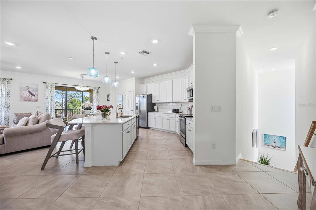 A bright, open-concept kitchen features white cabinetry, a large island, and light tile flooring — 10039 CROOKED CREEK DRIVE UNIT 201, VENICE, FL