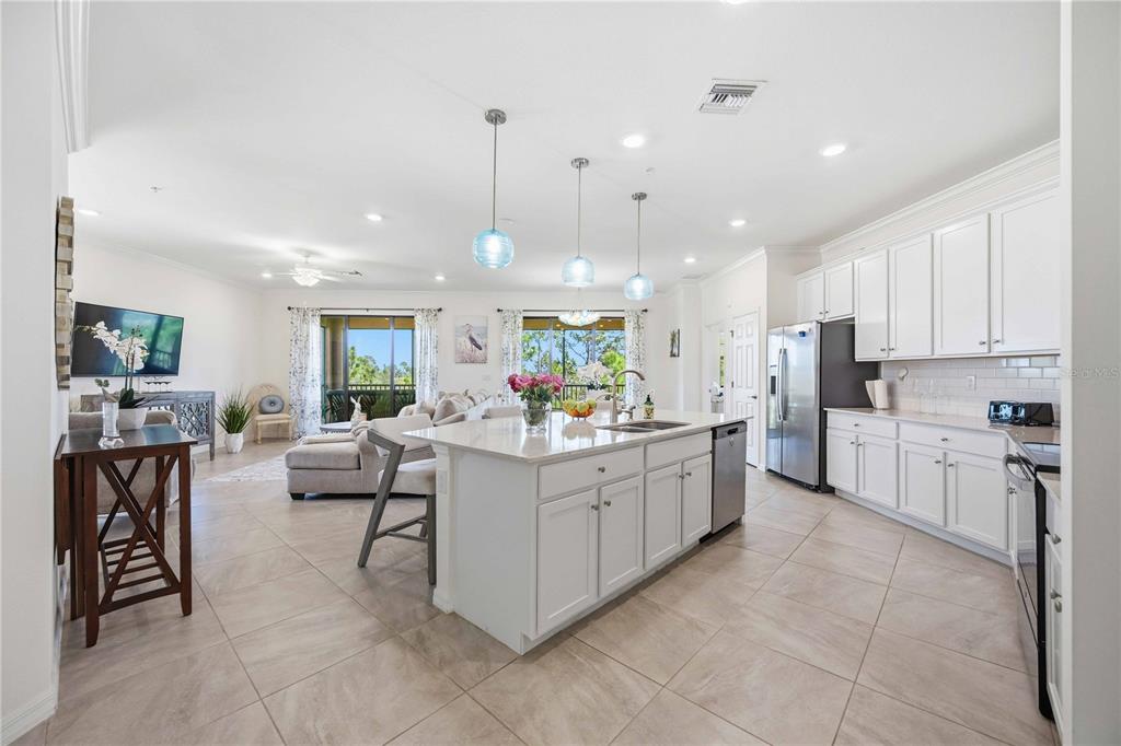 An open-concept kitchen and living area features white cabinetry, a central island, and tile flooring — 10039 CROOKED CREEK DRIVE UNIT 201, VENICE, FL