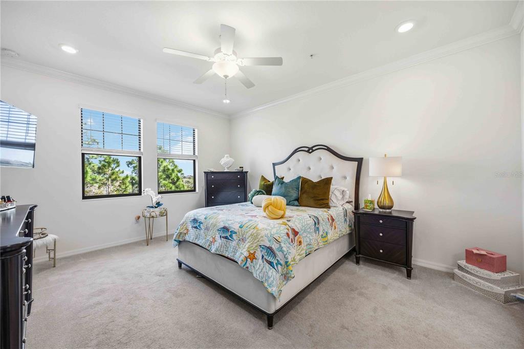 A bedroom features a bed with a patterned quilt, a ceiling fan, and two windows — 10039 CROOKED CREEK DRIVE UNIT 201, VENICE, FL