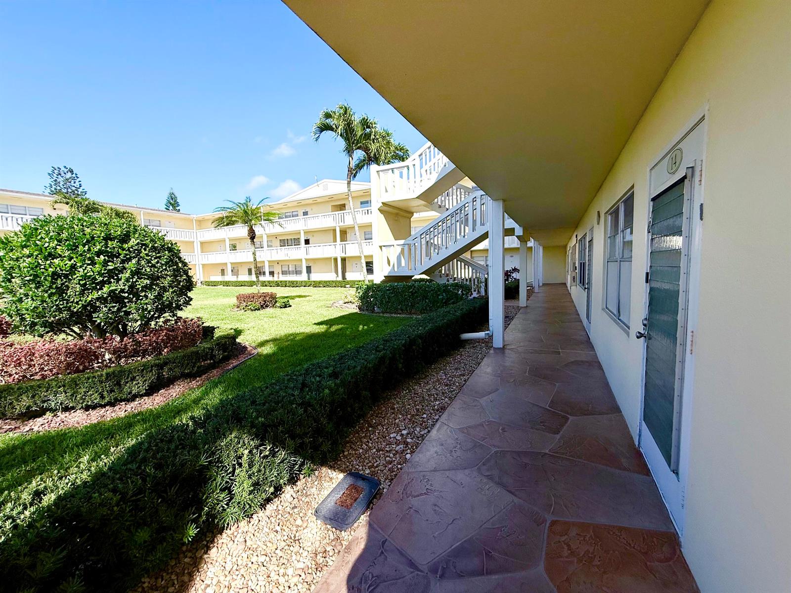 An exterior walkway with stone flooring leads past apartment doors toward a central courtyard — 13 Dorset A, Boca Raton FL 33434, BOCA RATON, FL