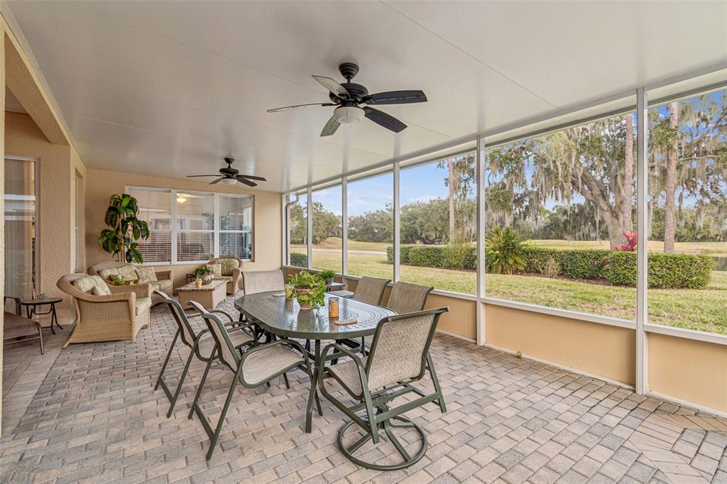 A screened-in patio features a dining set, wicker furniture, and views of a grassy landscape — 305 ROCK SPRINGS DRIVE, KISSIMMEE, FL