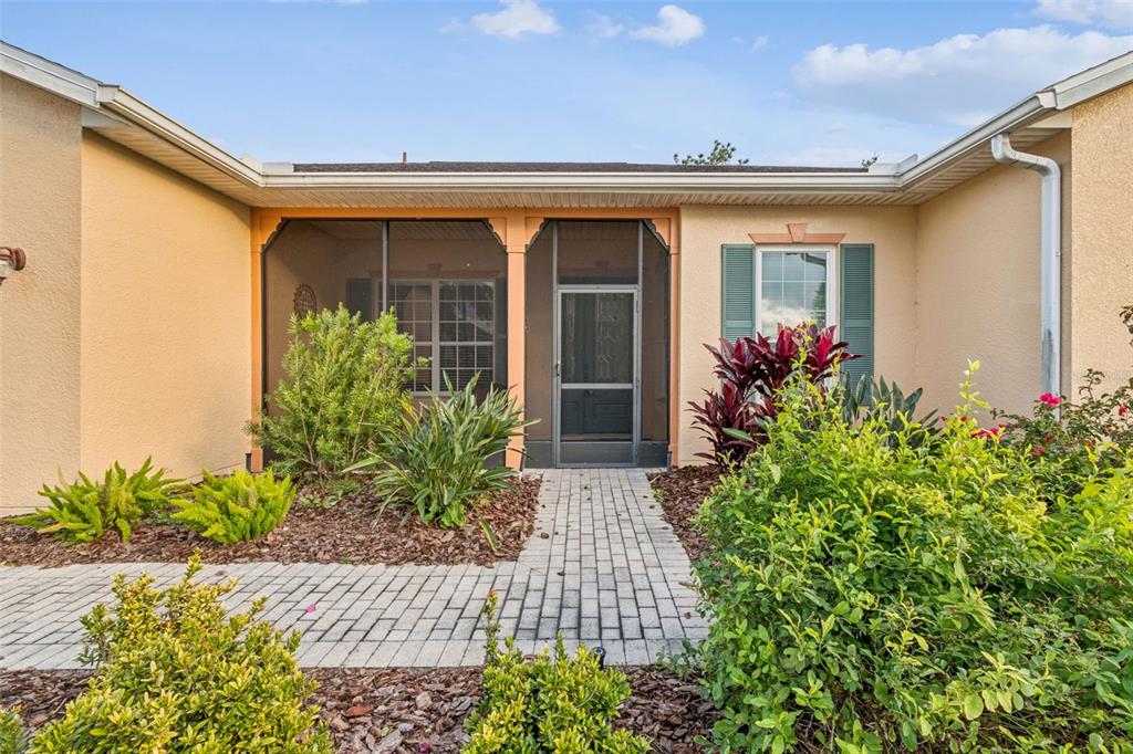 A paved walkway leads to the screened-in front entryway of a single-story stucco house — 305 ROCK SPRINGS DRIVE, KISSIMMEE, FL