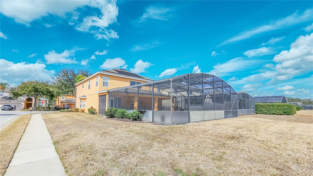 The exterior of a two-story yellow house features a large screened-in pool enclosure — 1009 ORANGE COSMOS BOULEVARD, DAVENPORT, FL