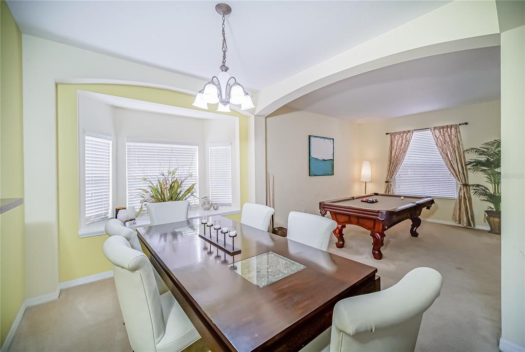 A dining room with a wooden table and white chairs sits adjacent to a pool room — 1009 ORANGE COSMOS BOULEVARD, DAVENPORT, FL