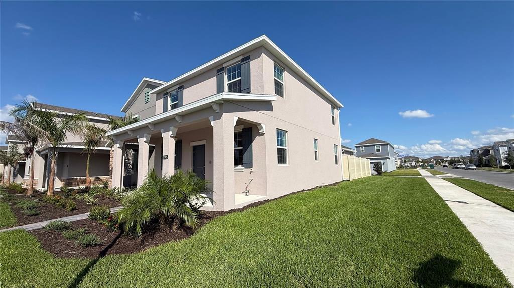 A two-story house with a covered porch and a side lawn under a blue sky — 1905 FULFILLMENT DRIVE, KISSIMMEE, FL