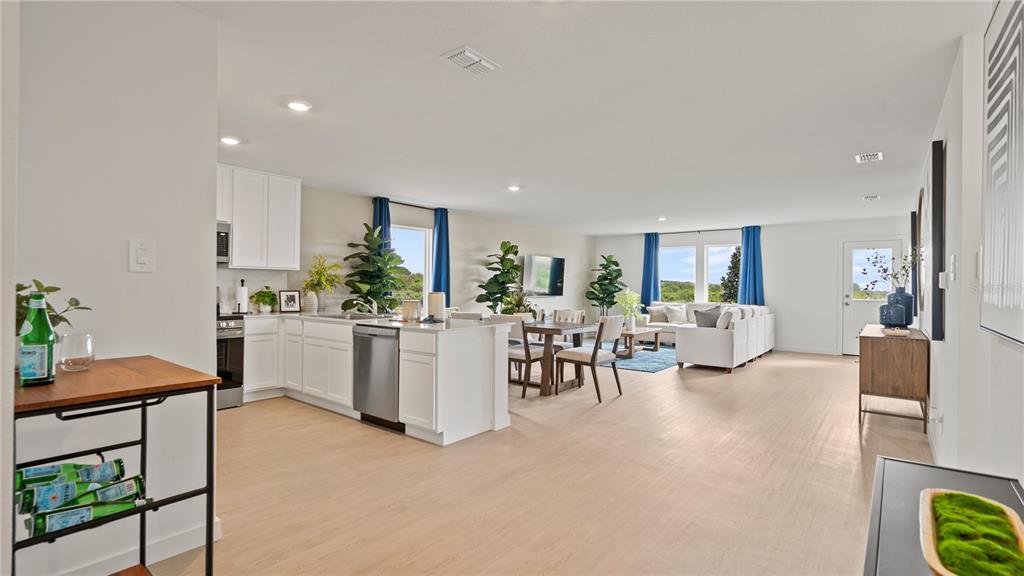 An open-concept kitchen and living area features white cabinetry, light wood flooring, and blue curtains — 1211 STETSON AVENUE, DUNDEE, FL