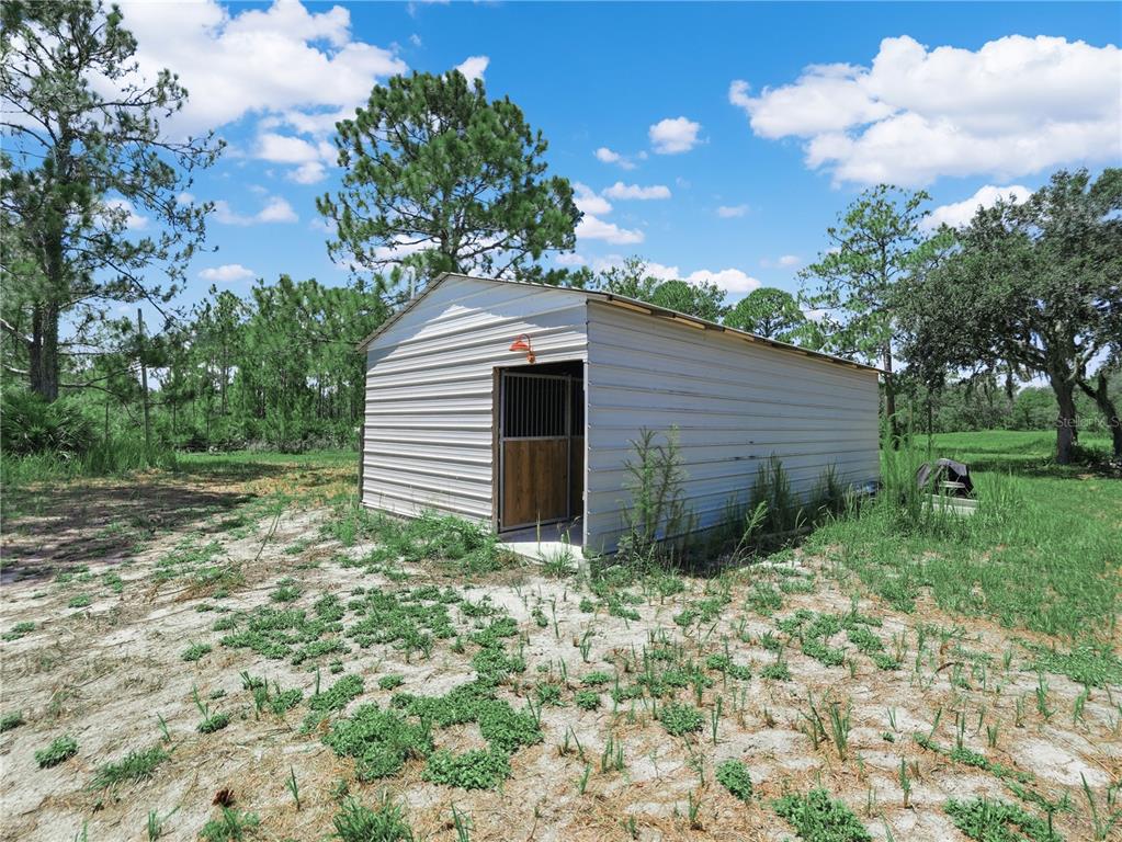 A metal shed with a horse stall door stands in a grassy, wooded outdoor area — 1202 R E BYRD RD, FROSTPROOF, FL