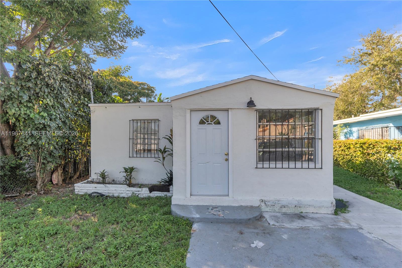A small, white, single-story house features a front door, two barred windows, and a yard — 6940 NW 6th Ct # 2, Miami FL 33150, MIAMI, FL