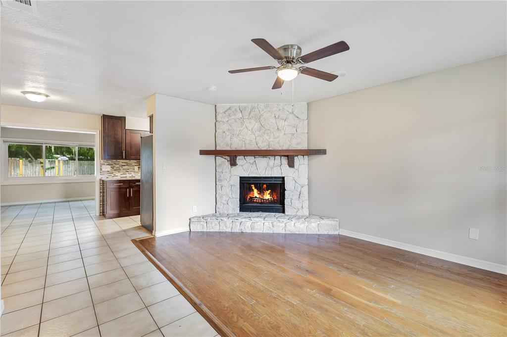 A living room features a corner stone fireplace, wood flooring, and an adjacent tiled kitchen — 1111 CABALLERO ROAD, OCOEE, FL