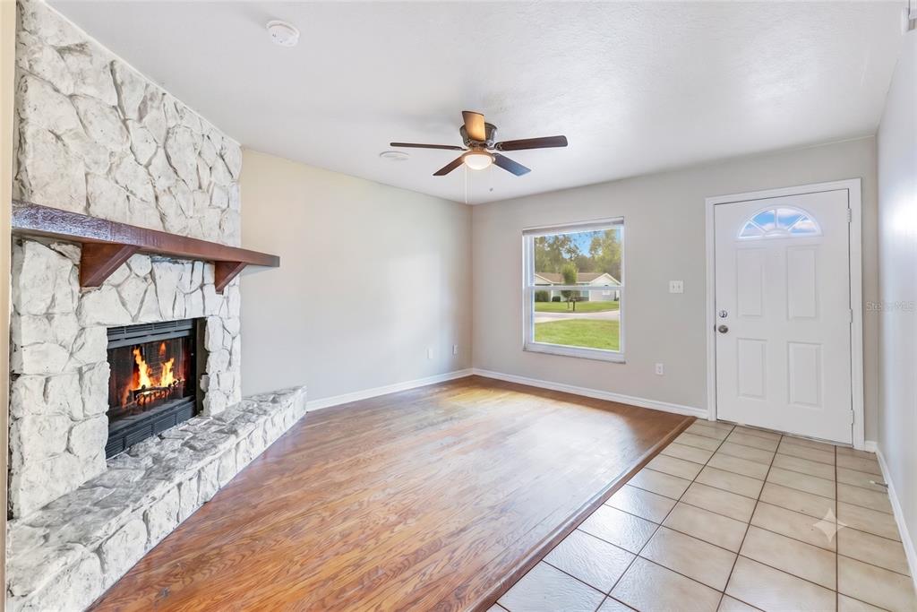 A living room features a stone fireplace, wood flooring, a ceiling fan, and a tiled entryway — 1111 CABALLERO ROAD, OCOEE, FL