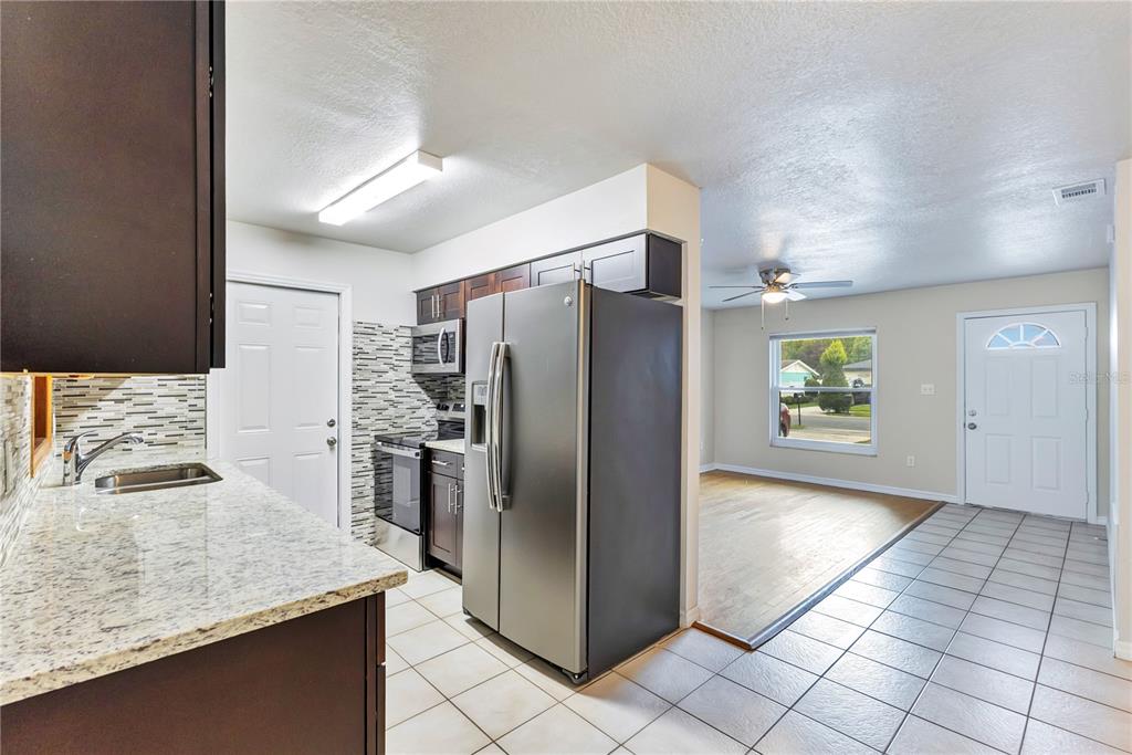A kitchen with granite countertops and stainless steel appliances opens into a living area — 1111 CABALLERO ROAD, OCOEE, FL