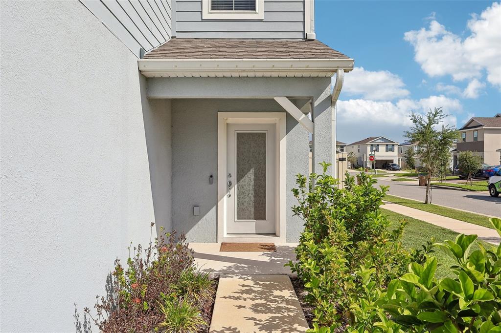 A concrete walkway leads to the front entrance of a house with light-colored siding — 5016 BLUE HAMMOCK COURT, KISSIMMEE, FL