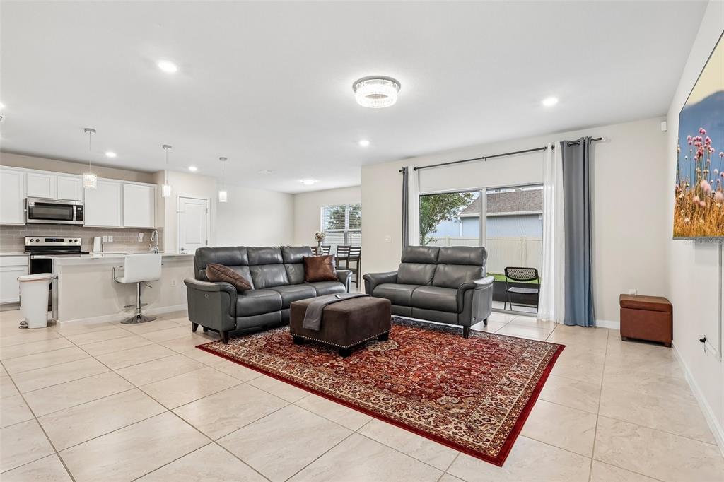 A living room with gray leather sofas, a red area rug, and an open kitchen — 5016 BLUE HAMMOCK COURT, KISSIMMEE, FL
