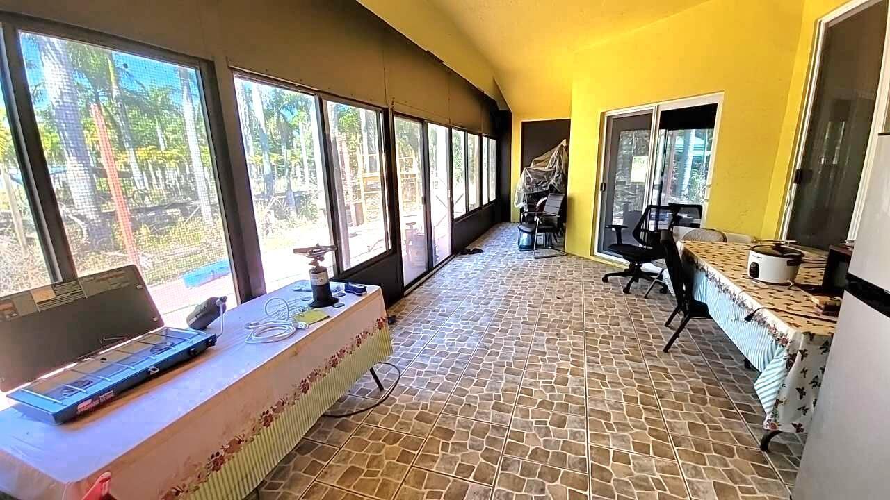 A sunroom features yellow walls, tiled flooring, and large windows overlooking a backyard — 4095 Windmill Road, Loxahatchee FL 33470, LOXAHATCHEE, FL