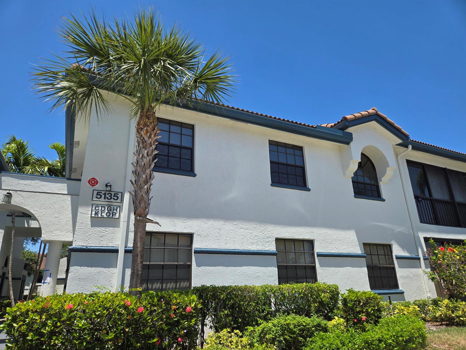 A two-story white stucco building with dark trim, a palm tree, and landscaping in front — 5135 Floria Drive # G, Boynton Beach FL 33437, BOYNTON BEACH, FL