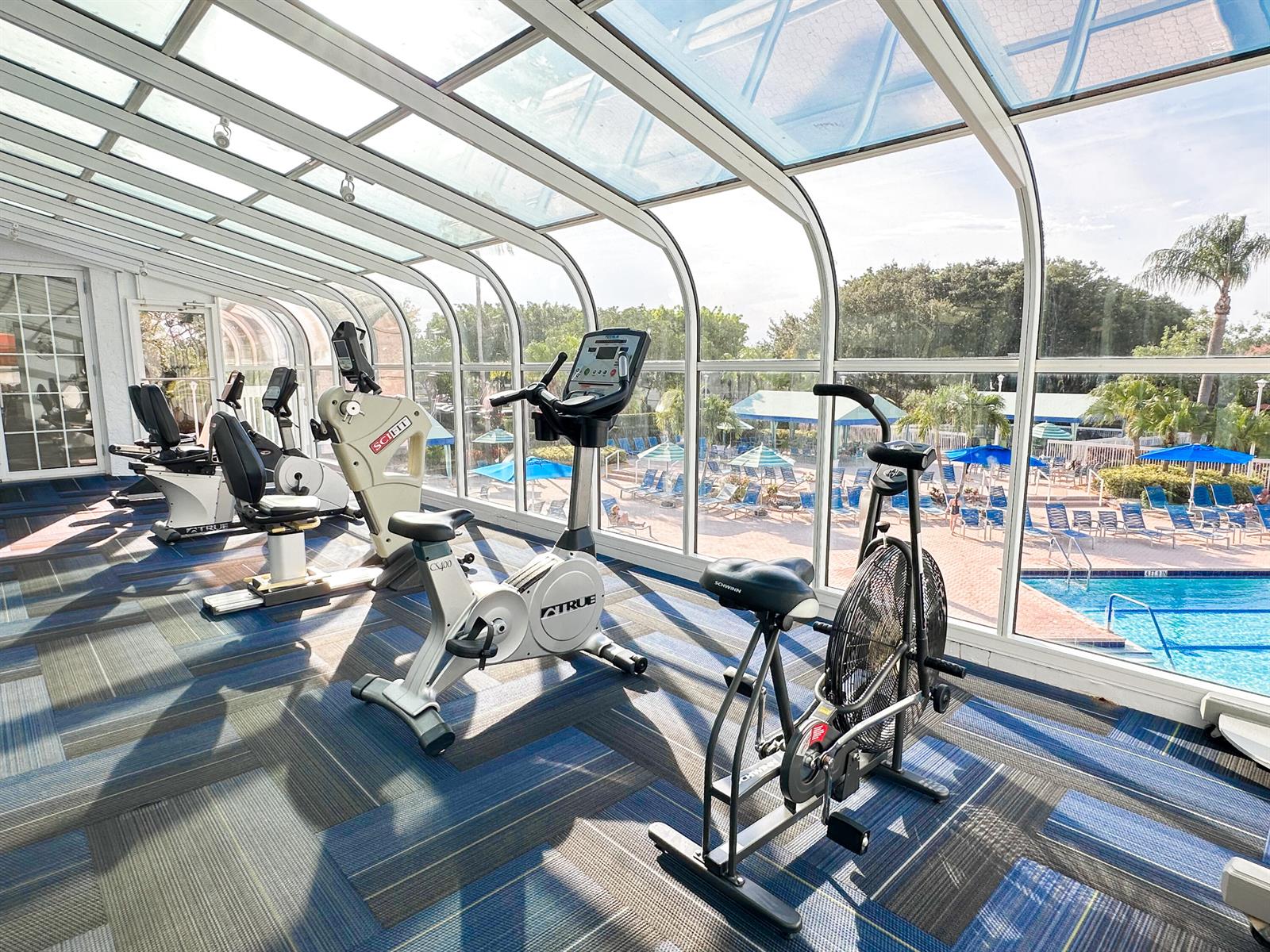 A gym with exercise bikes and a glass-enclosed ceiling overlooking an outdoor swimming pool — 5135 Floria Drive # G, Boynton Beach FL 33437, BOYNTON BEACH, FL