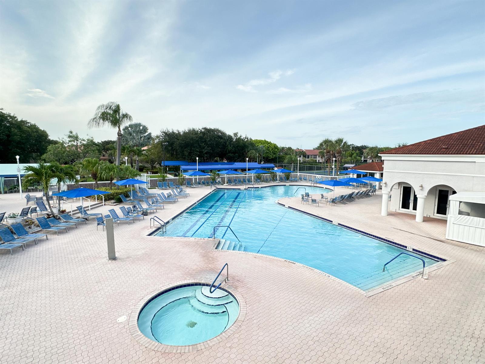 An outdoor swimming pool and hot tub are surrounded by a paved deck with umbrellas — 5135 Floria Drive # G, Boynton Beach FL 33437, BOYNTON BEACH, FL