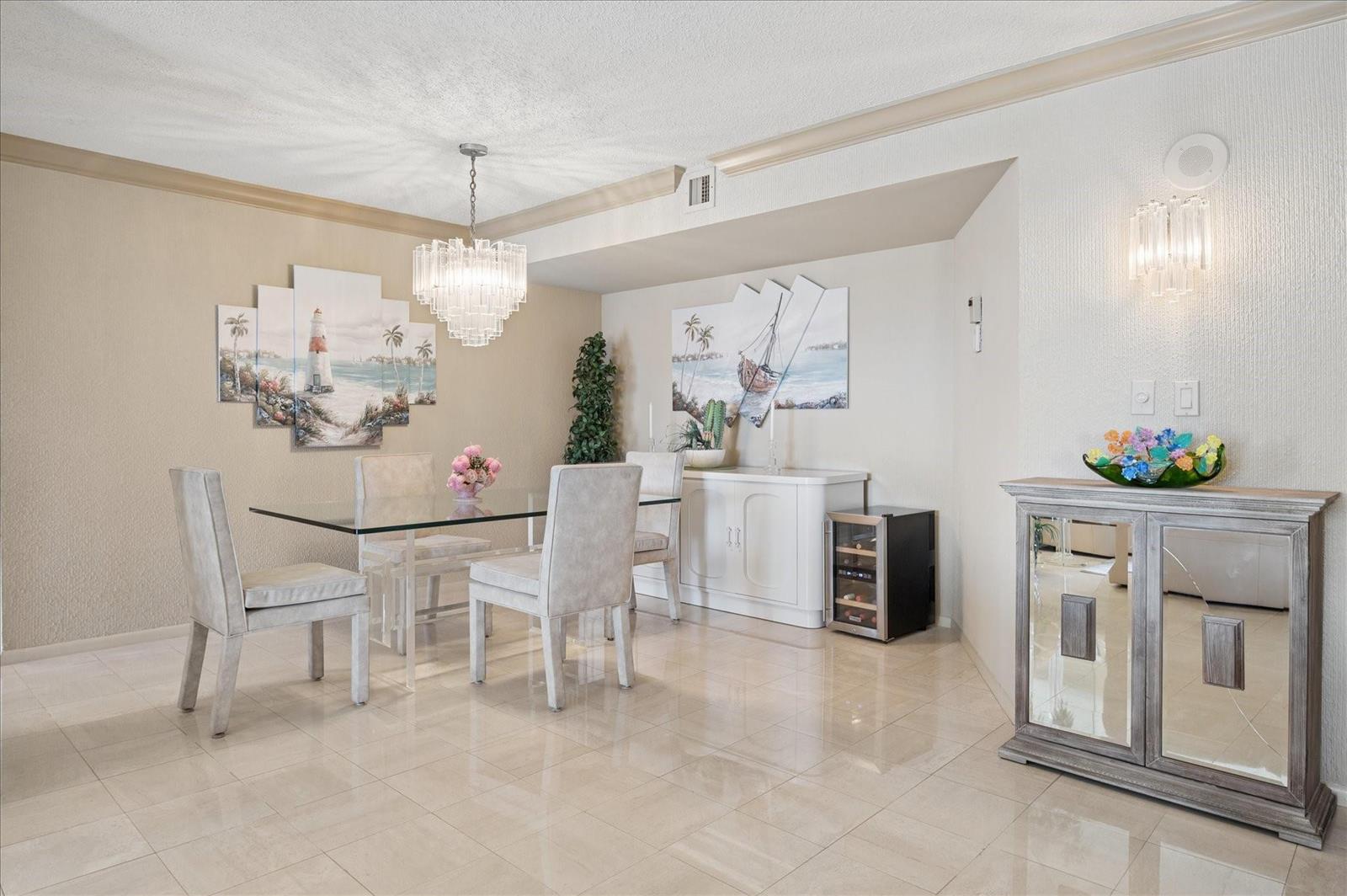 A dining room features a glass table, upholstered chairs, a crystal chandelier, and coastal artwork — 1201 S Ocean # 704s, Hollywood FL 33019, HOLLYWOOD, FL
