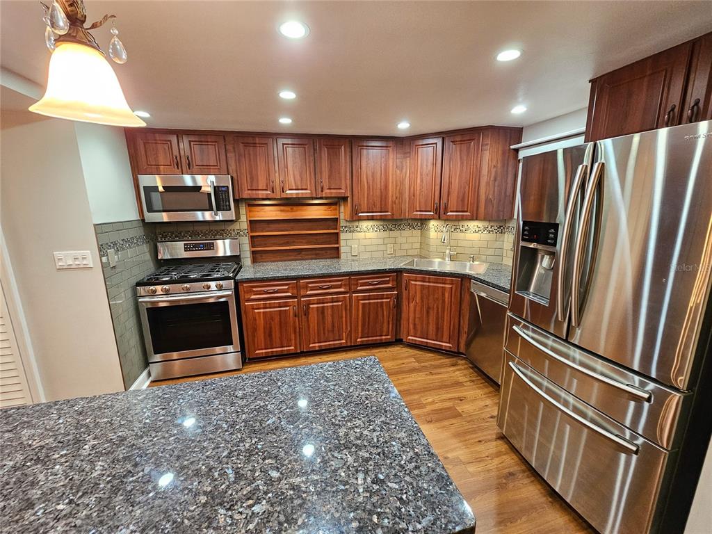 A kitchen features dark wood cabinets, granite countertops, stainless steel appliances, and a tiled backsplash — 6020 SHORE BOULEVARD S UNIT 701, GULFPORT, FL