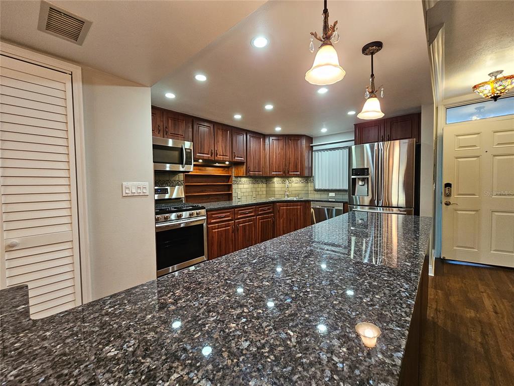 A kitchen features dark wood cabinets, granite countertops, stainless steel appliances, and recessed lighting — 6020 SHORE BOULEVARD S UNIT 701, GULFPORT, FL