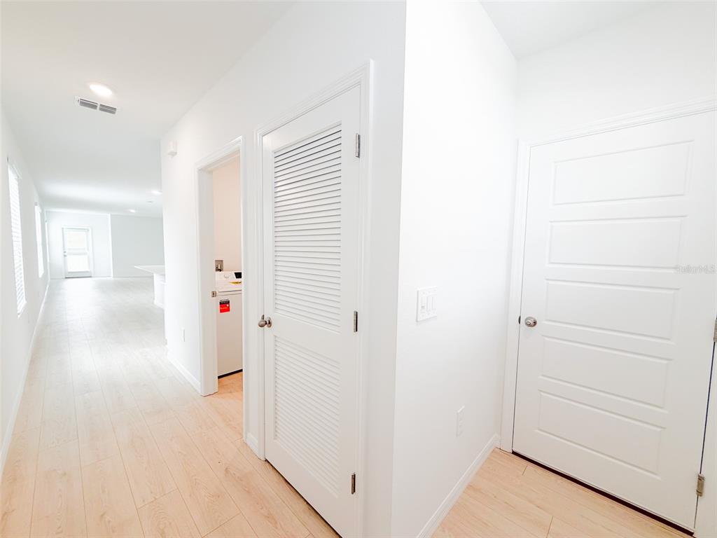 A hallway with light wood-look flooring leads to a laundry area and two white doors — 5168 NATIVE MILE LOOP, DAVENPORT, FL