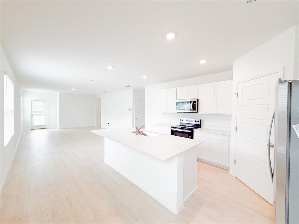 A bright, open-concept kitchen features white cabinetry, quartz countertops, a central island, and light flooring — 5168 NATIVE MILE LOOP, DAVENPORT, FL