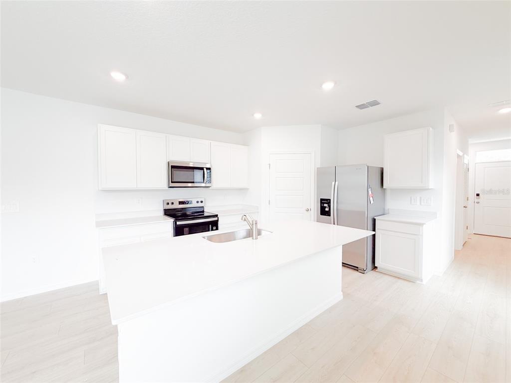 A modern kitchen features white cabinetry, stainless steel appliances, and a central island with sink — 5168 NATIVE MILE LOOP, DAVENPORT, FL