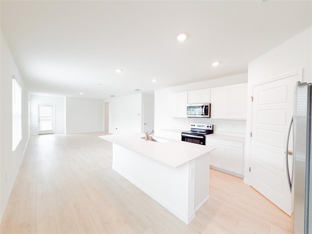 A bright, open-concept kitchen features white cabinetry, a central island, and light wood-look flooring — 5168 NATIVE MILE LOOP, DAVENPORT, FL