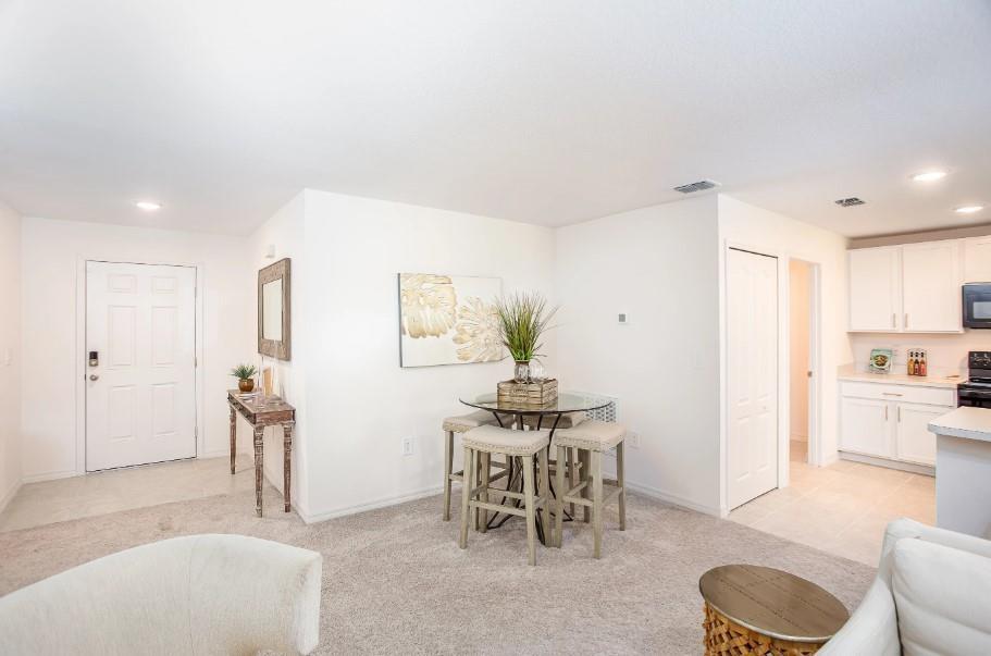 A dining area with a glass table and four stools sits near a white kitchen — 1394 Schumann Drive, Sebastian FL 32958, SEBASTIAN, FL